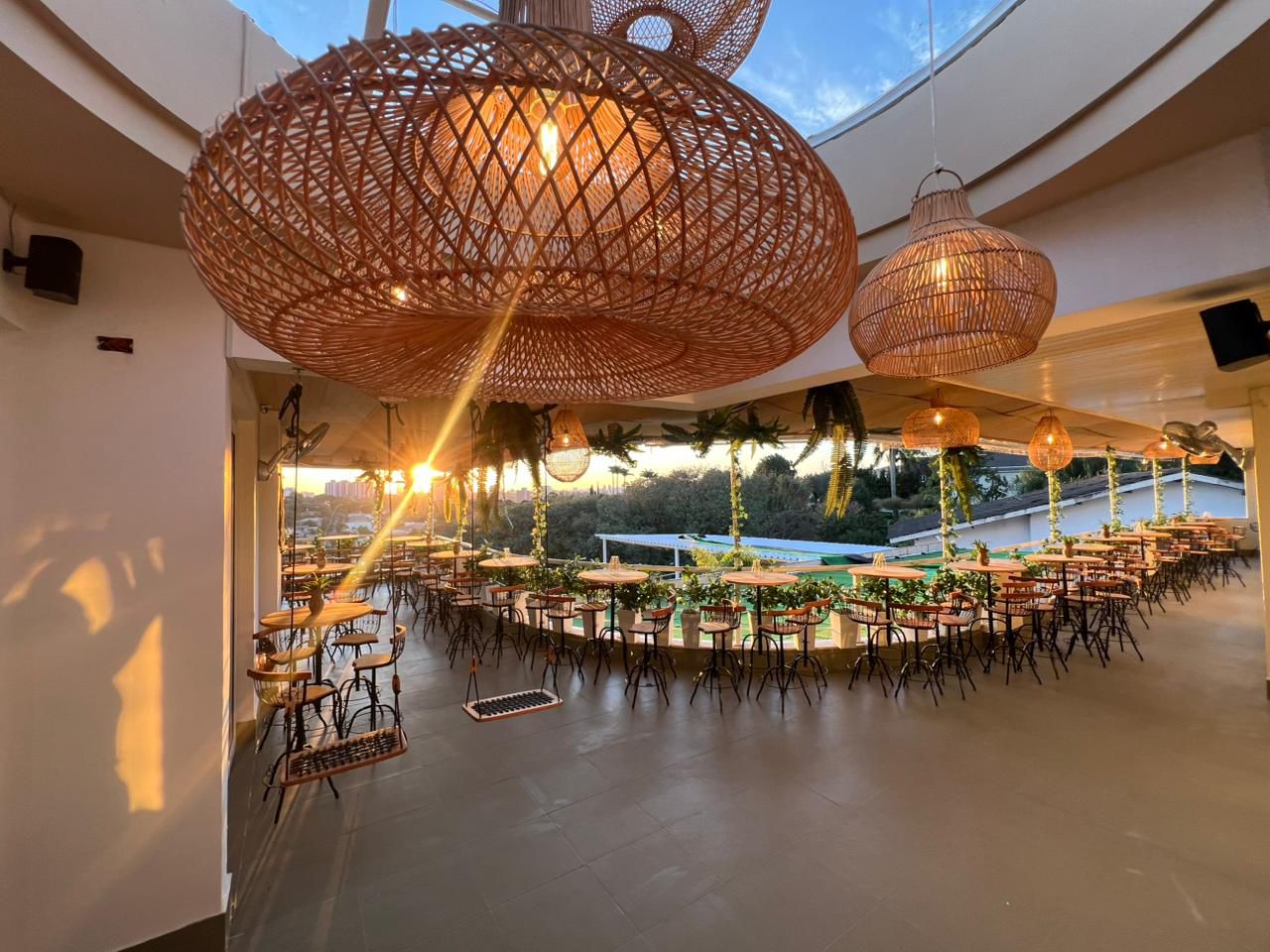 Espaço do evento ao entardecer, com lustres de vime e mesa montada